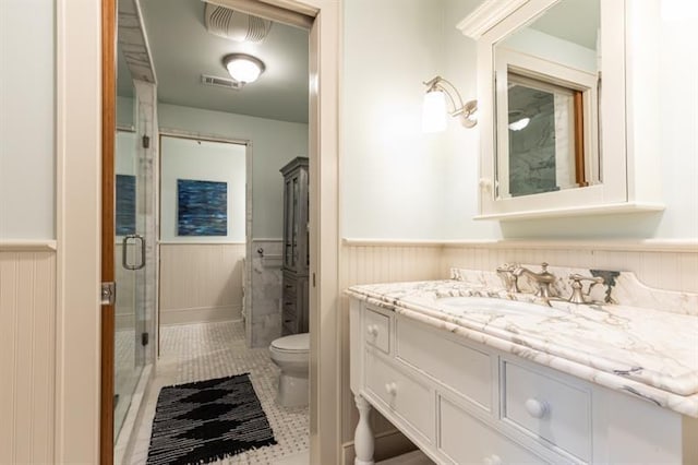 bathroom featuring a wainscoted wall, toilet, a shower stall, and vanity