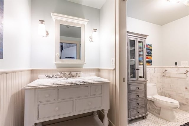 half bathroom featuring a wainscoted wall, vanity, toilet, and tile patterned floors