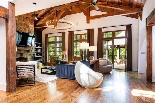 living area with ceiling fan with notable chandelier, a stone fireplace, wood finished floors, and wood ceiling