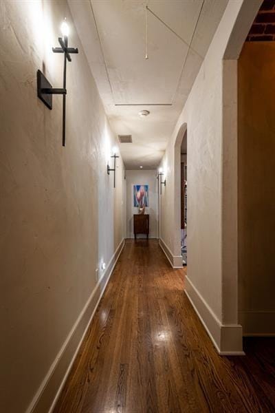corridor with baseboards, attic access, arched walkways, and wood finished floors
