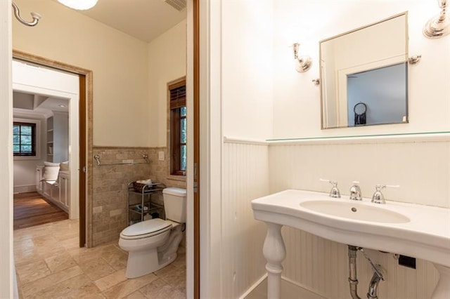 bathroom with toilet, visible vents, tile walls, and wainscoting