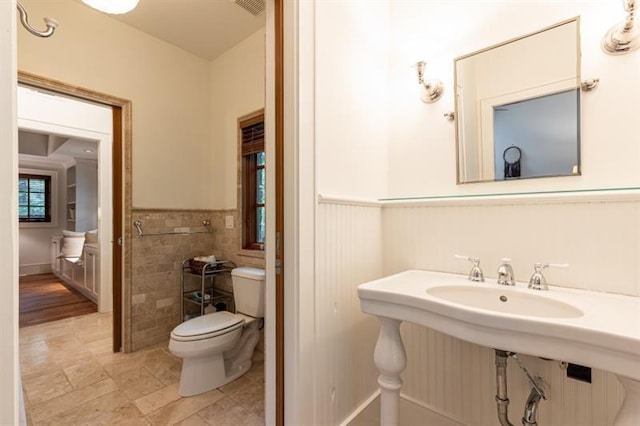 half bath with visible vents, a wainscoted wall, tile walls, and toilet