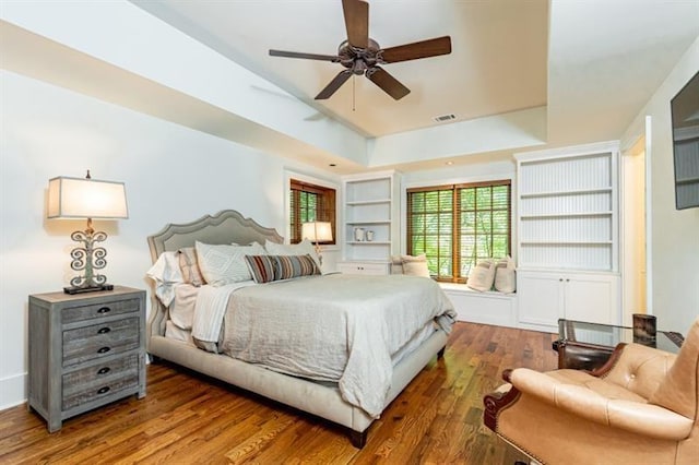 bedroom featuring a ceiling fan, visible vents, a raised ceiling, and wood finished floors