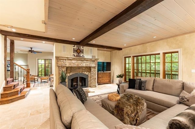 living room featuring beamed ceiling, stone tile flooring, a stone fireplace, plenty of natural light, and stairs