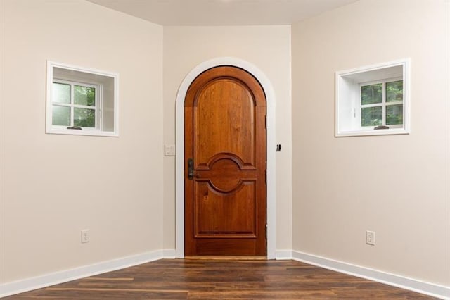entrance foyer featuring baseboards, arched walkways, and dark wood-style flooring