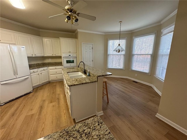 kitchen with hanging light fixtures, sink, white cabinets, white appliances, and a center island with sink