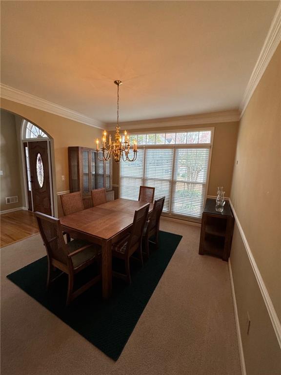 carpeted dining space featuring crown molding and a notable chandelier