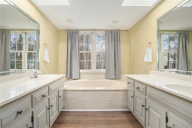 bathroom with hardwood / wood-style flooring, vanity, a washtub, and a skylight