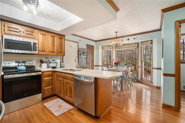 kitchen with appliances with stainless steel finishes, sink, hanging light fixtures, light hardwood / wood-style floors, and kitchen peninsula