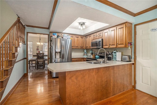 kitchen featuring appliances with stainless steel finishes, sink, a notable chandelier, light hardwood / wood-style floors, and kitchen peninsula