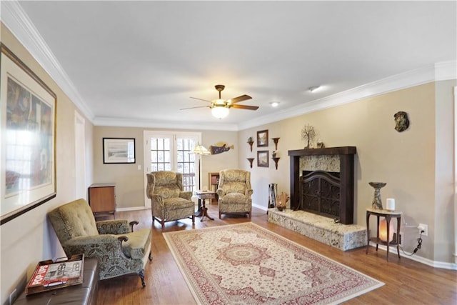 living area featuring baseboards, a ceiling fan, ornamental molding, wood finished floors, and a fireplace