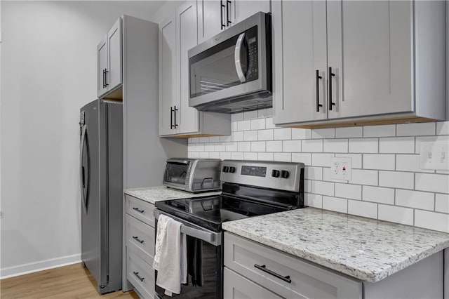 kitchen with light hardwood / wood-style floors, light stone countertops, appliances with stainless steel finishes, gray cabinets, and backsplash