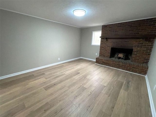 unfurnished living room featuring a brick fireplace, crown molding, light hardwood / wood-style flooring, and a textured ceiling