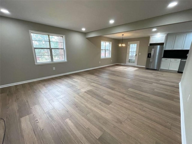 unfurnished living room featuring an inviting chandelier and light wood-type flooring