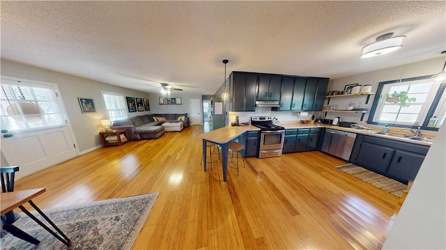 kitchen featuring blue cabinets, under cabinet range hood, stainless steel appliances, a sink, and open shelves