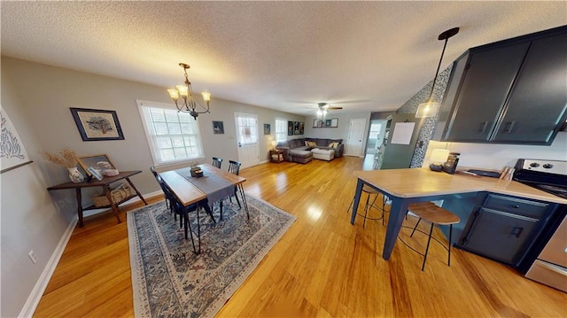 dining area featuring a textured ceiling, ceiling fan with notable chandelier, light wood-type flooring, and baseboards