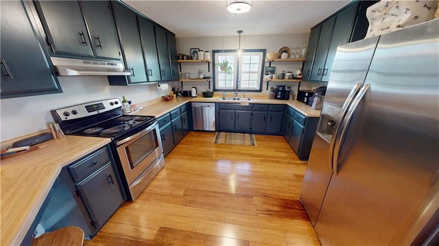 kitchen with light wood-style floors, stainless steel appliances, under cabinet range hood, open shelves, and a sink