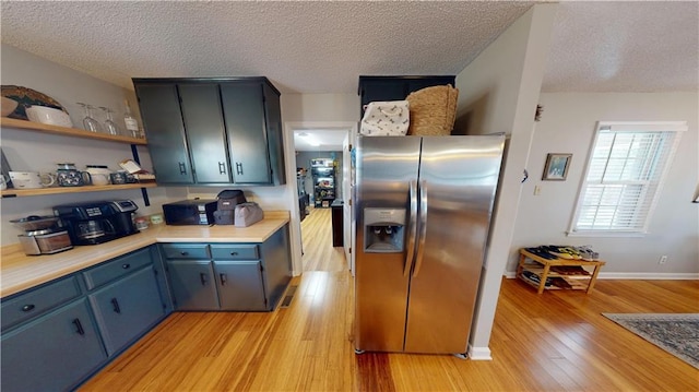 kitchen featuring light countertops, blue cabinetry, light wood-type flooring, stainless steel refrigerator with ice dispenser, and open shelves