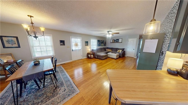 dining space featuring a textured ceiling, ceiling fan with notable chandelier, baseboards, and light wood-style floors