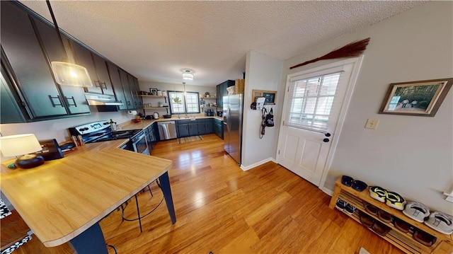 kitchen with open shelves, light countertops, appliances with stainless steel finishes, light wood-style floors, and under cabinet range hood