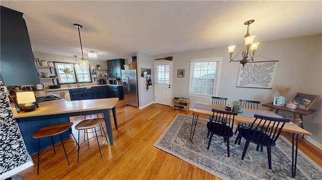 dining room featuring light wood-style floors, a notable chandelier, a textured ceiling, and baseboards