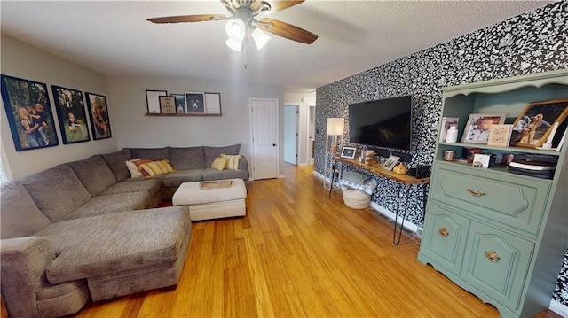 living room with wallpapered walls, a ceiling fan, an accent wall, a textured ceiling, and light wood-type flooring