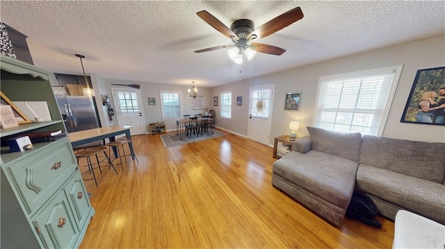 living room with light wood-type flooring, baseboards, a ceiling fan, and a textured ceiling