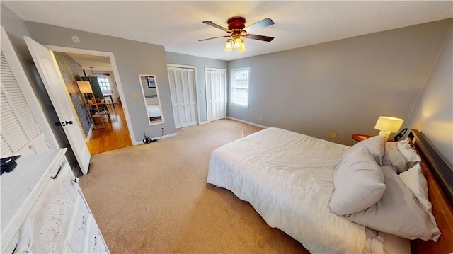 bedroom featuring a ceiling fan, light colored carpet, baseboards, and two closets