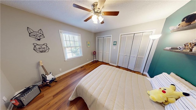 bedroom featuring a textured ceiling, wood finished floors, a ceiling fan, baseboards, and multiple closets