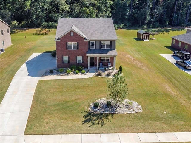 colonial-style house with driveway, brick siding, an outbuilding, a porch, and a front yard