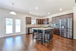 kitchen featuring dark wood finished floors, stainless steel appliances, wall chimney range hood, dark brown cabinets, and a kitchen breakfast bar