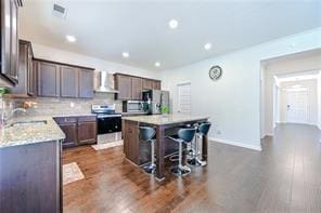 kitchen with wall chimney exhaust hood, a kitchen island, appliances with stainless steel finishes, a breakfast bar, and a sink