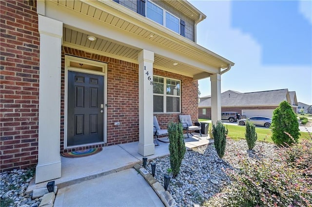 doorway to property featuring a porch and brick siding