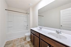 full bathroom featuring toilet, double vanity,  shower combination, and a sink