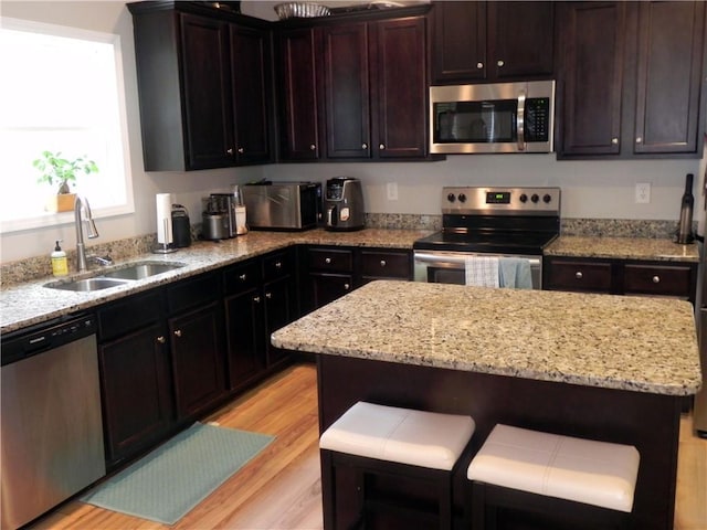 kitchen with light stone counters, sink, stainless steel appliances, and a center island