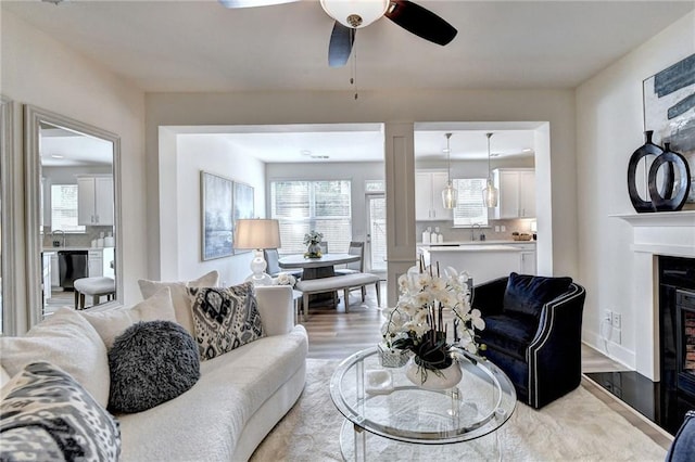 living area with light wood-style floors, a glass covered fireplace, a healthy amount of sunlight, and ceiling fan