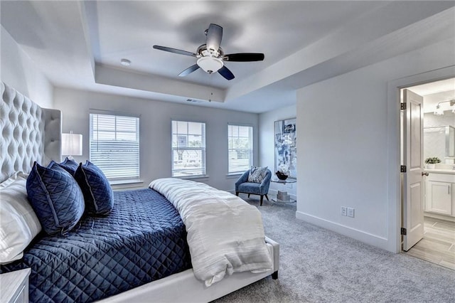 bedroom featuring light colored carpet, a tray ceiling, multiple windows, and baseboards