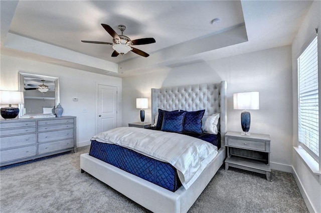 carpeted bedroom with baseboards, a tray ceiling, and ceiling fan