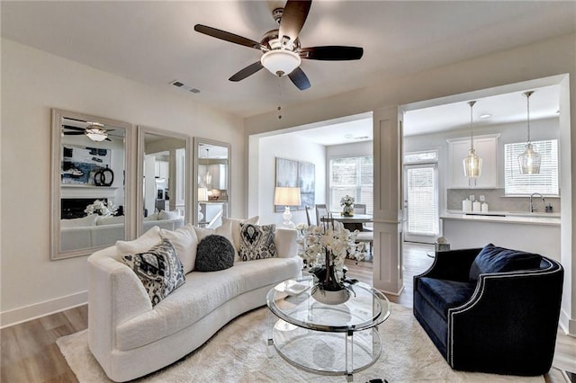 living area featuring a ceiling fan, visible vents, baseboards, and wood finished floors