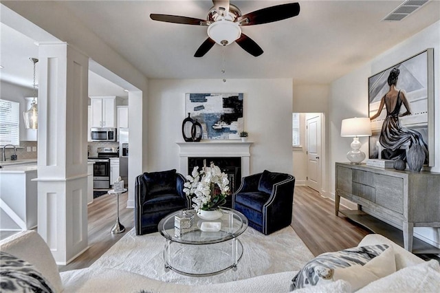 living area featuring visible vents, ceiling fan, ornate columns, light wood-style floors, and a fireplace