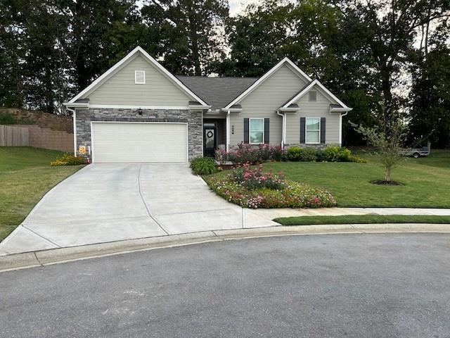 single story home featuring stone siding, concrete driveway, and a front yard