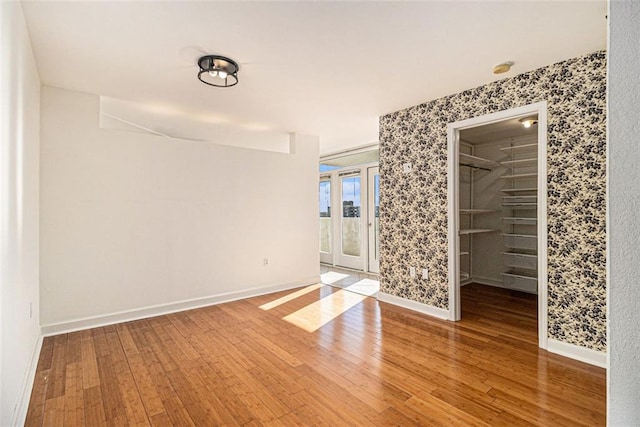 empty room featuring wallpapered walls, baseboards, and wood-type flooring