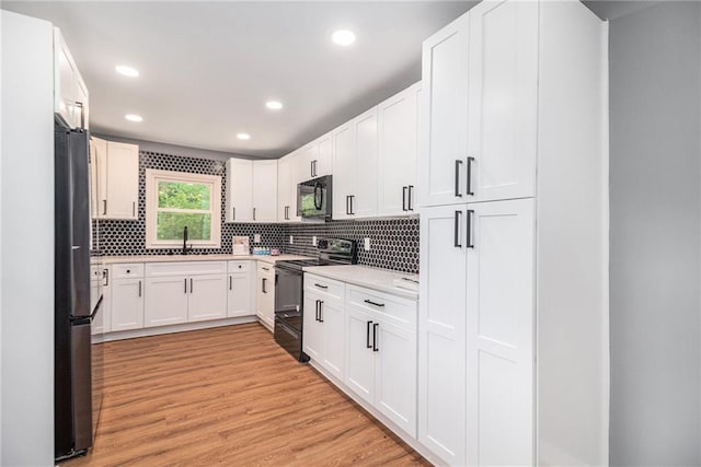 kitchen featuring decorative backsplash, a sink, black appliances, and light wood-style floors