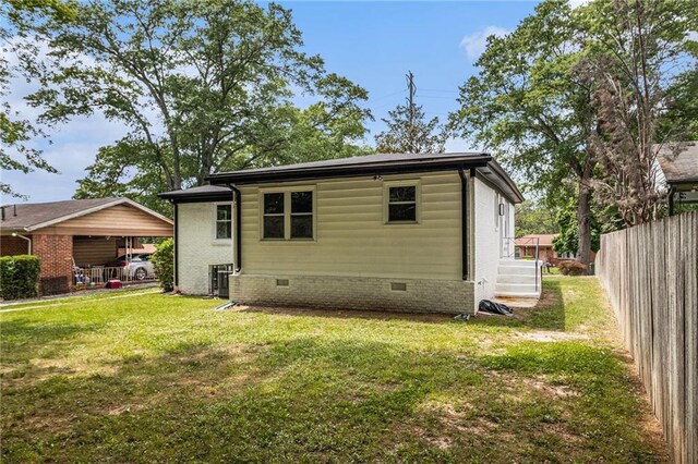 rear view of house featuring fence, a lawn, and crawl space