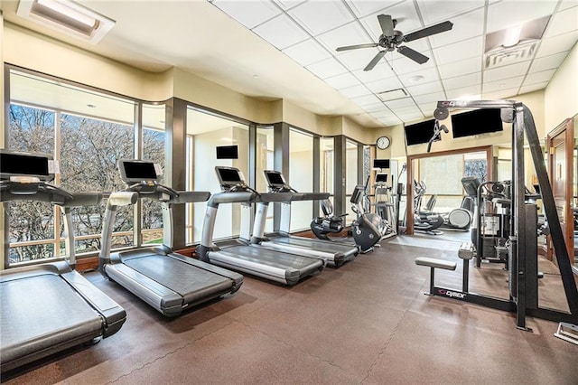 gym featuring ceiling fan, plenty of natural light, and a drop ceiling