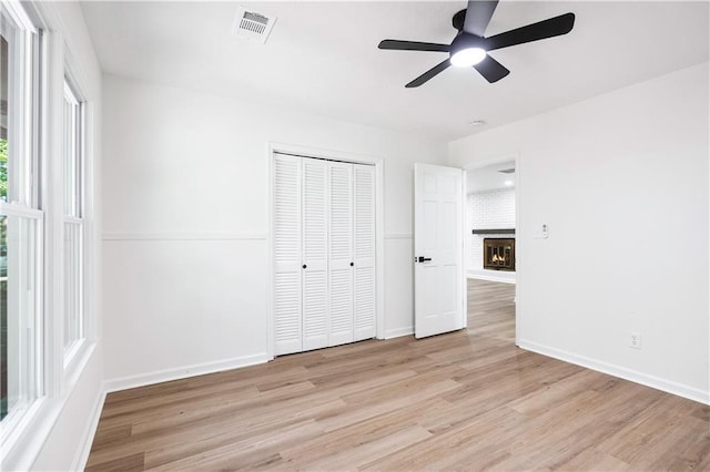 unfurnished bedroom featuring a brick fireplace, light hardwood / wood-style floors, a closet, and ceiling fan