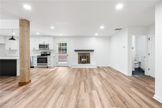 unfurnished living room with a brick fireplace and light hardwood / wood-style floors