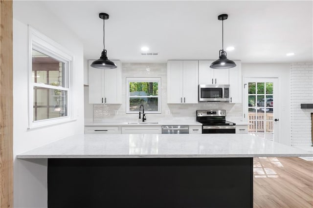 kitchen with appliances with stainless steel finishes, sink, hanging light fixtures, and white cabinets