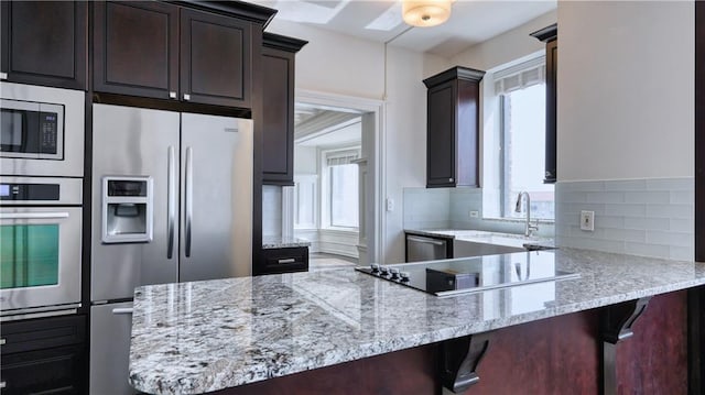 kitchen with light stone countertops, kitchen peninsula, stainless steel appliances, and backsplash