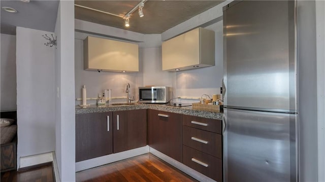 kitchen with track lighting, sink, dark brown cabinetry, appliances with stainless steel finishes, and dark wood-type flooring